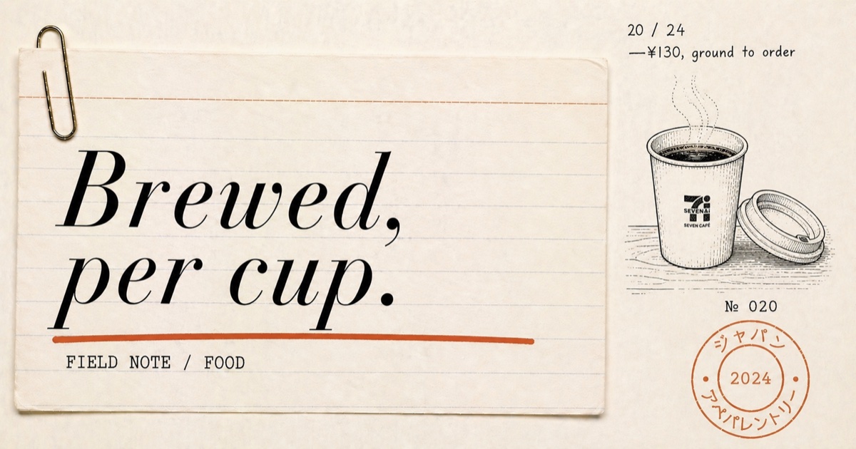 A paper cup of freshly brewed coffee on the counter of a Japanese 7-Eleven, the bean-to-cup machine visible behind it with a green label reading SEVEN CAFE
