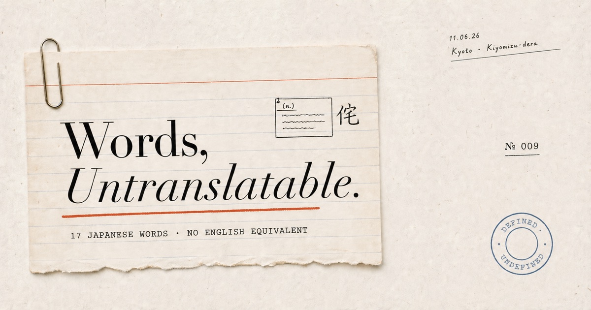 A handwritten Japanese phrasebook open on a wooden café table beside a small ceramic cup of green tea, with cherry-blossom petals drifting onto the page where the words 木漏れ日 and 侘寂 are written in black ink